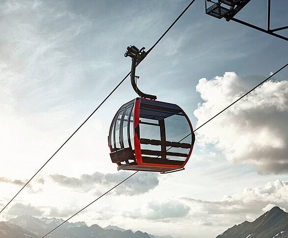 A modern gondola cabin suspended against a bright sky above the mountains